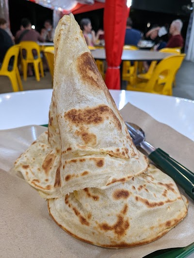 Stacked roti canai, a flaky Indian-influenced flatbread served at AL-JALAL BY Habib's Rojak restaurant with yellow chairs visible in background. — Items: Roti Canai