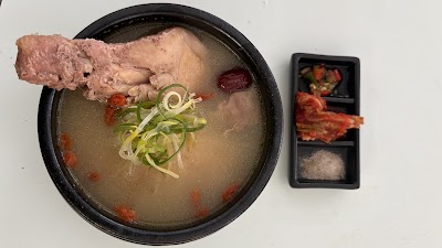 OMMA Chicken Soup served in a black bowl with tender chicken, green onion garnish, and side condiments including gochugaru and salt. — Items: Chicken Soup