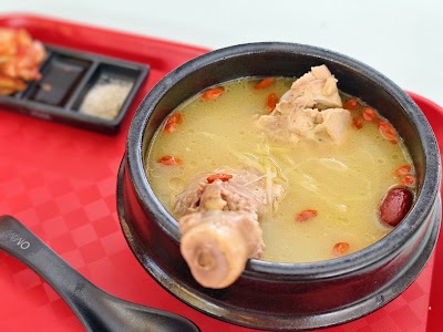 OMMA Chicken Soup served in a dark bowl with tender chicken pieces, red chili peppers, and clear broth on a red placemat. — Items: Chicken Soup
