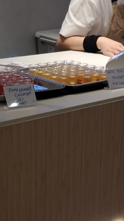 Cha Mulan tea shop beverage samples display featuring Pomegranate Collagen and White Peach Collagen drinks in small cups with handwritten price labels. — Items: Pomegranate Collagen 25元 · White Peach Collagen 50%糖
