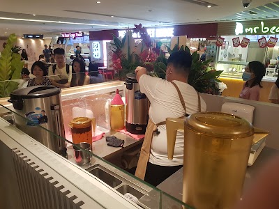 Cha Mulan tea shop counter displaying various tea beverages including iced and hot tea in glass dispensers and metal teapots in a shopping mall setting. — Items: Tea beverages · Iced tea · Hot tea