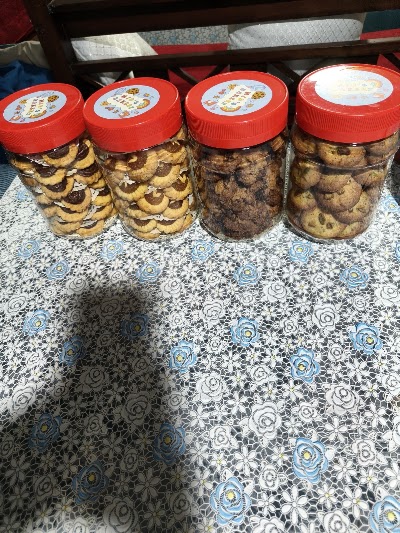 Four jars of Mid's Bakery cookies with red lids containing chocolate chip cookies, chocolate cookies, butter cookies, and mixed cookies displayed on a decorative tablecloth. — Items: Chocolate Chip Cookies · Chocolate Cookies · Butter Cookies · Mixed Cookies