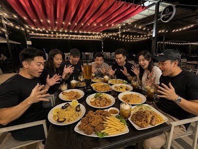 Group dining at Chickyfish restaurant with fried chicken, fries, spaghetti, fried noodles, garlic noodles, and seafood pasta dishes served on white plates under red awning with string lights. — Items: Fried Chicken with Fries · Spaghetti · Fried Noodles · Garlic Noodles · Seafood Pasta · Fried Rice