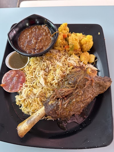 Persian Tandoor grilled lamb chop with saffron rice, fried cauliflower, dal lentils, salami, and traditional sauces on a black plate — Items: Grilled Lamb Chop · Saffron Rice · Fried Cauliflower · Dal Lentils · Salami · Brown Sauce/Gravy · Light Sauce/Yogurt Sauce