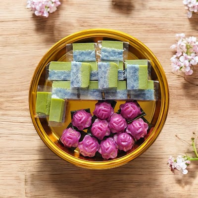 Assorted Nonya kueh in gold tin: pandan custard cakes with green and blue striping, and decorative pink rose-shaped pastries from Kueharmony. — Items: Pandan Custard Cake (Green and Blue Striped) · Pandan Custard Cake (Green and Gray Striped) · Rose-shaped Kueh (Pink/Magenta)