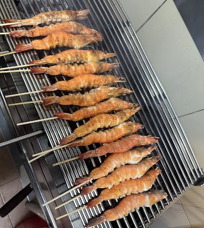 Grilled shrimp skewers and satay cooking on barbecue grill at M BBQ Wings & Satay restaurant — Items: Grilled Shrimp Skewers · Satay