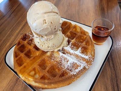Golden waffle dusted with powdered sugar topped with two scoops of vanilla ice cream, served with syrup on the side at Lickers restaurant. — Items: Waffle with Vanilla Ice Cream · Syrup