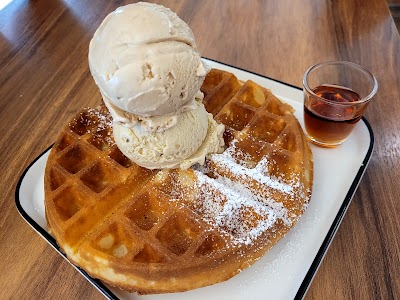 Golden waffle topped with powdered sugar and two scoops of vanilla ice cream, served with syrup on the side at Lickers restaurant. — Items: Waffle with Vanilla Ice Cream · Syrup