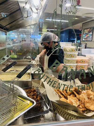 Authentic Thai restaurant counter at Talad Thai Banana displaying fried chicken, pad thai noodles, and other Thai dishes in metal serving containers with staff preparing food behind protective glass. — Items: Fried Chicken · Thai Noodles · Pad Thai