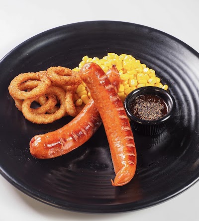 Bradley's Grill plate with two grilled sausages, crispy onion rings, corn, and dipping sauce on black plate — Items: Grilled Sausages · Onion Rings · Corn