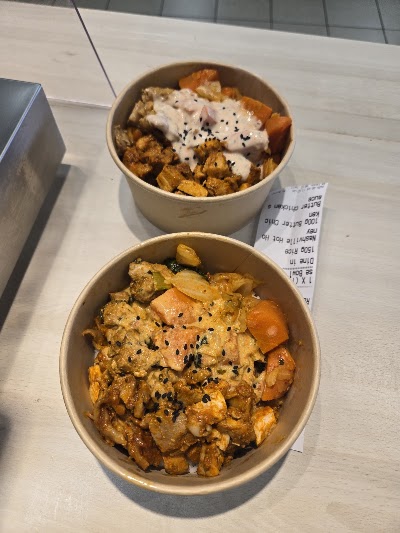 Two Asian rice bowls from N2 No Nonsense Foods: curry rice with chicken and creamy sauce topped with sesame seeds, and fried chicken with potatoes and black sesame garnish. — Items: Curry Rice Bowl with Chicken and Sauce · Fried Chicken with Potato and Sesame Seeds
