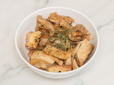 Seasoned chicken slices served in a white bowl, garnished with fresh herbs and black pepper, presented on a marble surface. — Items: Chicken Slices