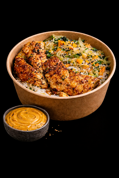 Grilled chicken rice bowl with vegetables and black sesame seeds served with spiced orange sauce in a paper container. — Items: Grilled Chicken Rice Bowl · Spiced Sauce