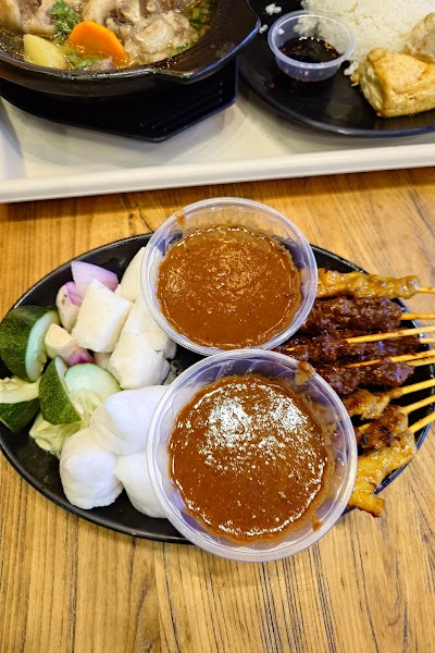 Loka Loka Ang Mo Kio dining spread featuring satay skewers with peanut sauce, fresh vegetable platter, meat stew, and rice with dipping sauce — Items: Satay Skewers · Peanut Sauce · Vegetable Platter with Cucumber and Onions · Stew or Soup with Meat and Vegetables · Rice · Dipping Sauce