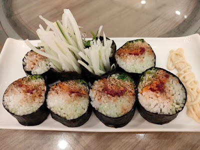 Sushi rolls with nori, filled with spiced tuna and rice, garnished with cucumber slices and served with wasabi at Yes Natural Restaurant. — Items: Sushi Roll with Spicy Tuna · Cucumber Salad · Wasabi