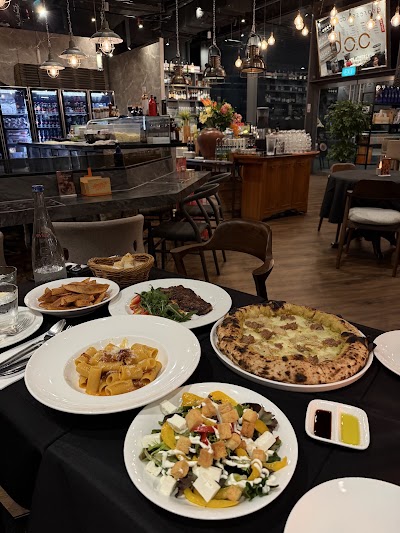 d.o.c Italian Restaurant table spread featuring pappardelle pasta, grilled steak, wood-fired pizza, salad with croutons and cheese, fried potatoes, and bread basket. — Items: Pappardelle with meat sauce · Grilled steak with greens · Pizza with bacon and cheese · Salad with croutons, cheese, and vegetables · Fried potatoes · Bread basket