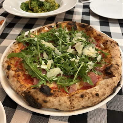Wood-fired pizza topped with prosciutto, fresh arugula, and shaved parmesan at d.o.c Italian Restaurant, served with a side of broccoli with garlic. — Items: Prosciutto and Arugula Pizza · Broccoli with Garlic