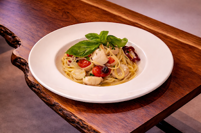 Spaghetti with scallops and cherry tomatoes garnished with fresh basil, served on a white plate at d.o.c Italian Restaurant. — Items: Spaghetti with Scallops and Cherry Tomatoes