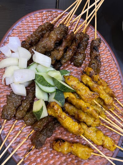 Grilled beef and chicken satay skewers served with sliced onions and cucumber on a decorative plate at Haryati's restaurant. — Items: Beef Satay · Chicken Satay