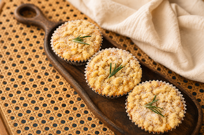 Three golden rosemary muffins with fresh rosemary garnish served on a wooden board at The Dessert Party. — Items: Rosemary Muffin