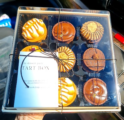 The Dessert Party Tart Box featuring assorted gourmet tarts including lemon, salted caramel, pistachio, passion fruit, chocolate, and coffee varieties in an elegant presentation box. — Items: Lemon Tart · Salted Caramel Tart · Pistachio Tart · Passion Fruit Tart · Chocolate Tart · Coffee Tart · Chocolate Mousse Tart