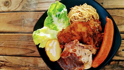 Roger's Kitchen grilled meat platter with fried noodles, fresh lettuce, boiled potatoes, and grilled red pepper served on a black plate. — Items: Grilled Meat Platter · Fried Noodles · Lettuce · Boiled Potatoes · Grilled Red Pepper