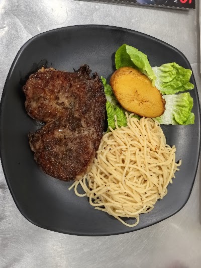 Roger's Kitchen grilled steak served with spaghetti pasta, grilled potato, and fresh lettuce salad on a black plate. — Items: Grilled Steak · Spaghetti Pasta · Grilled Potato · Lettuce Salad