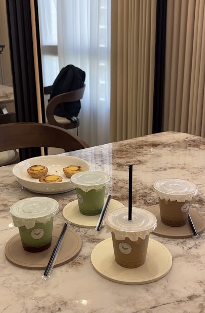 Mama Matcha table spread featuring matcha lattes, coffee lattes, and egg tarts served in branded cups with saucers and straws on a marble table. — Items: Matcha Latte · Coffee Latte · Egg Tarts