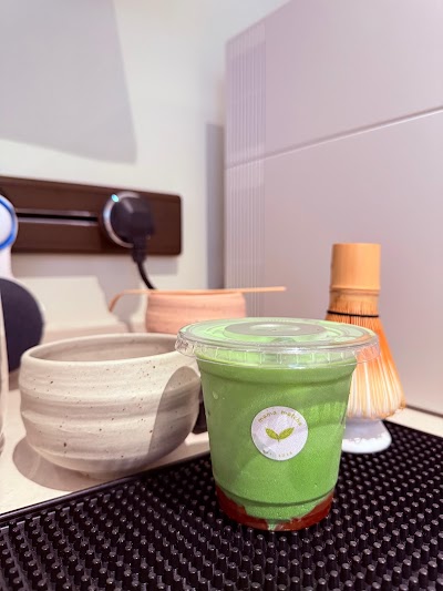Mama Matcha green matcha beverage in clear cup with logo sticker, served with ceramic matcha bowl and whisk on table. — Items: Matcha Drink
