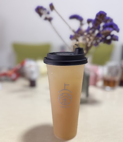 Shang Cha milk tea drink in takeaway cup with black lid, outdoor setting with purple flowers in background. — Items: Milk Tea Beverage