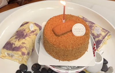 LadyLeFlour bakery desserts including Honey Cloud cake with candle, purple yam cake slices, and fresh blueberries on white plate. — Items: Honey Cloud Cake · Purple Yam Cake · Blueberries