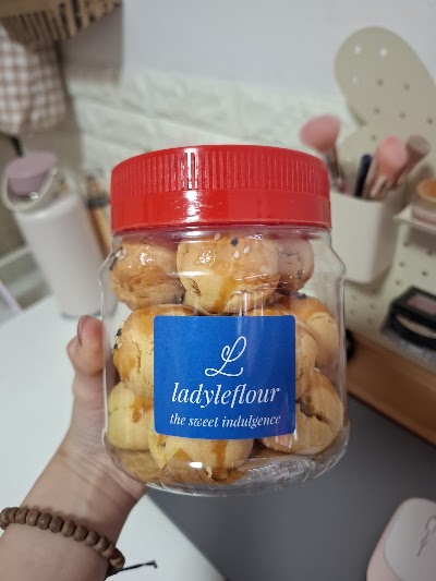 LadyLeFlour chocolate chip cookies in a glass jar with red lid, displaying the brand's 'the sweet indulgence' tagline on blue label. — Items: Chocolate Chip Cookies