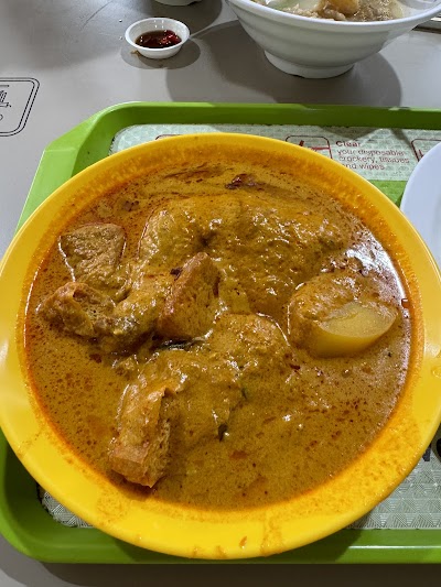 Masala Curry Chicken dish served in a yellow bowl with rich golden gravy, tender chicken pieces, and potatoes, accompanied by a small bowl of chili sauce. — Items: Masala Curry Chicken · Diced Pork Noodles