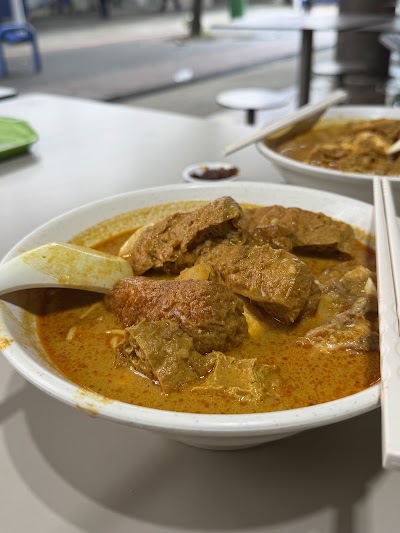 Masala Curry Chicken served in a rich, aromatic golden curry sauce with tender meat pieces in a white bowl at an outdoor restaurant setting. — Items: Curry Chicken