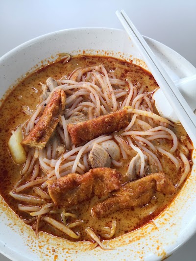 Masala Curry Chicken Noodle bowl with spiced red broth, thin noodles, chicken pieces, and seafood in a white ceramic speckled dish with chopsticks. — Items: Masala Curry Chicken Noodle